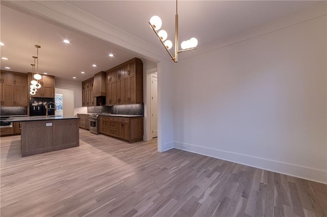 kitchen with an island with sink, wall chimney exhaust hood, tasteful backsplash, and stainless steel stove