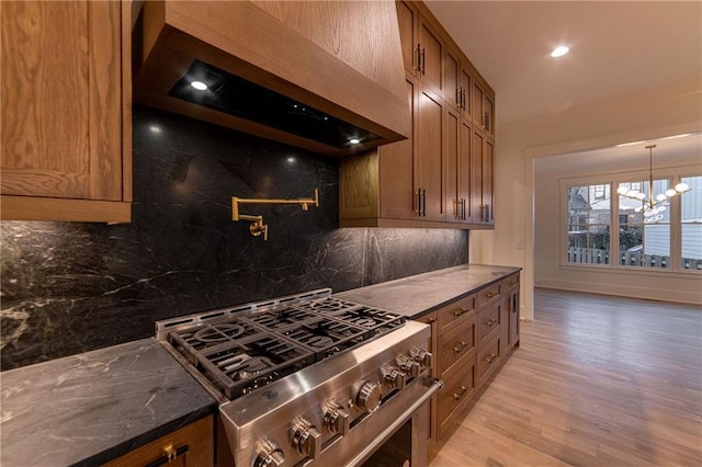 kitchen with brown cabinetry, custom exhaust hood, high end range, and light wood-style floors