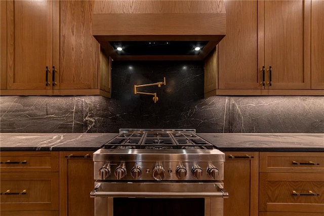 kitchen featuring brown cabinetry, backsplash, stainless steel range, and wall chimney range hood