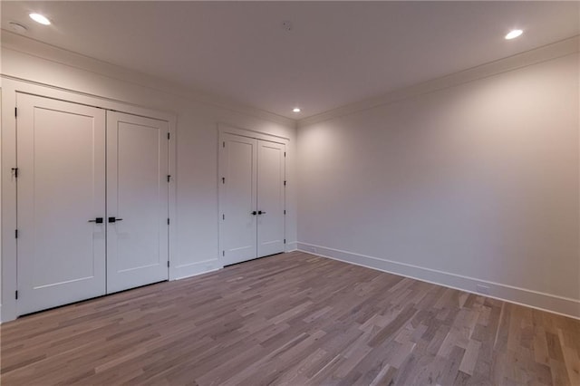 unfurnished bedroom featuring baseboards, ornamental molding, multiple closets, and wood finished floors