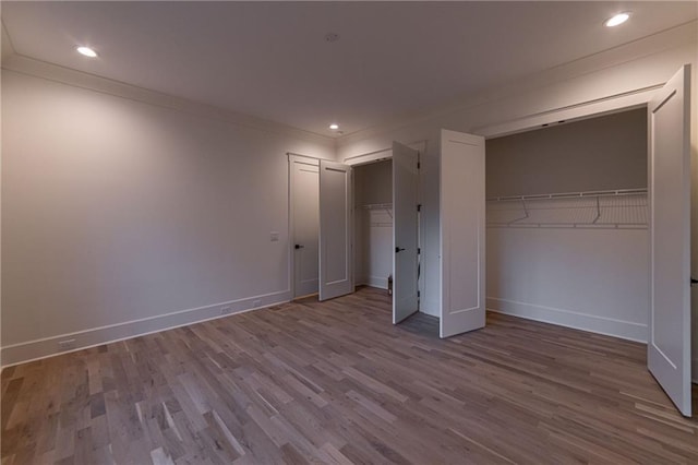 unfurnished bedroom featuring recessed lighting, wood finished floors, baseboards, and two closets