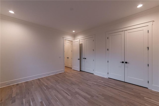 unfurnished bedroom featuring baseboards, wood finished floors, crown molding, multiple closets, and recessed lighting