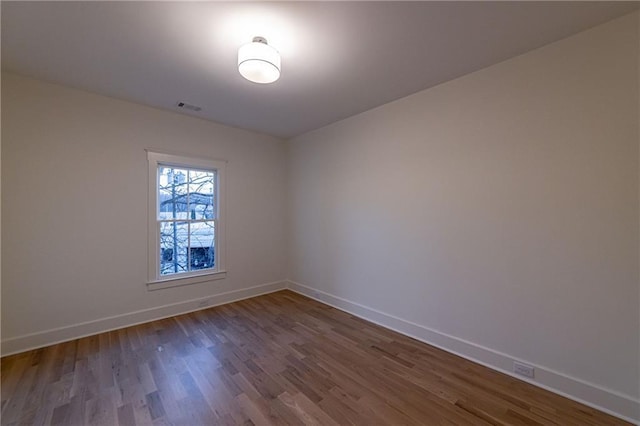 unfurnished room with baseboards, visible vents, and wood finished floors