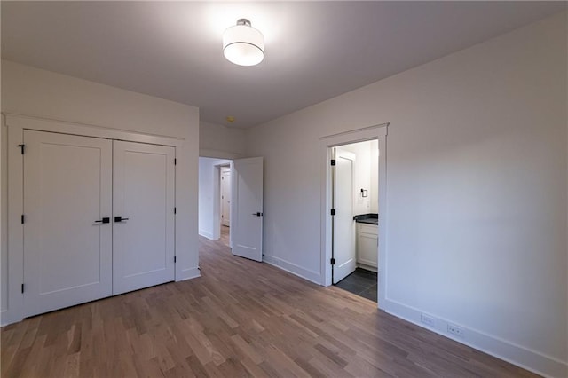 unfurnished bedroom with ensuite bathroom, a closet, wood finished floors, and baseboards