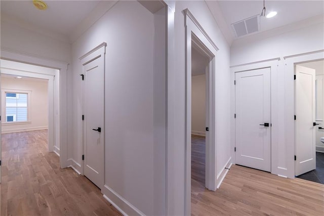 hall with light wood-style floors, visible vents, ornamental molding, and baseboards