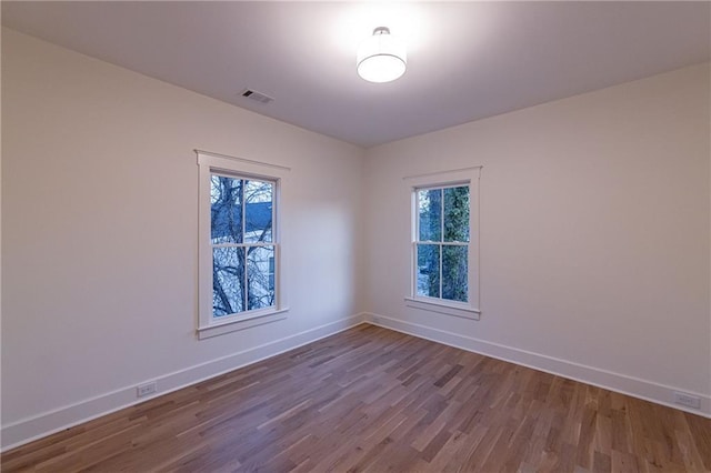 empty room featuring baseboards, visible vents, and wood finished floors