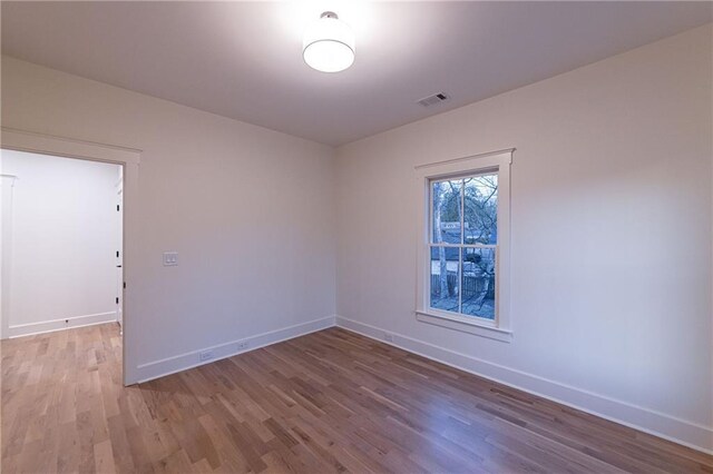 unfurnished room with wood finished floors, visible vents, and baseboards