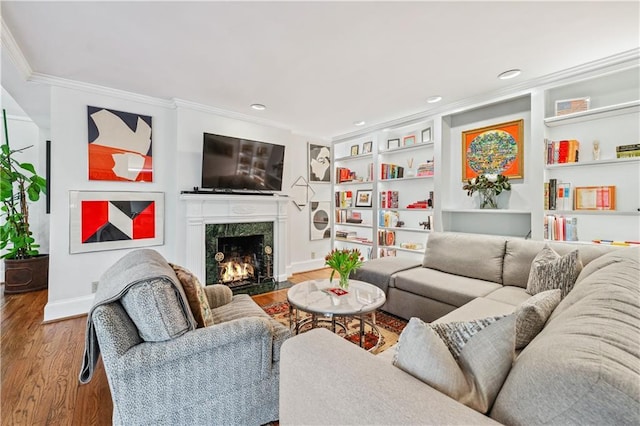living room featuring wood finished floors, baseboards, built in shelves, ornamental molding, and a high end fireplace