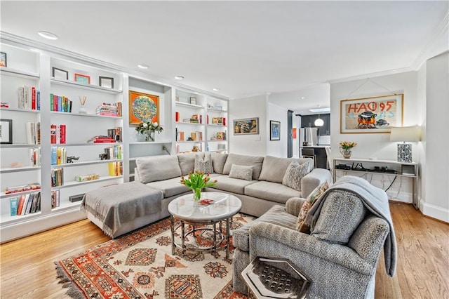 living room with light wood-style floors, built in shelves, baseboards, and ornamental molding