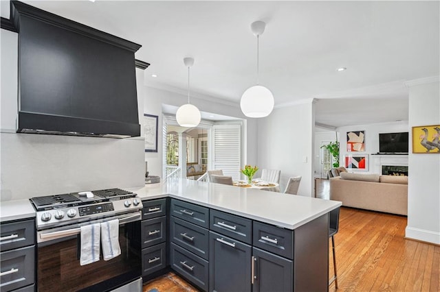 kitchen featuring a peninsula, a breakfast bar, wall chimney exhaust hood, gas range, and light countertops