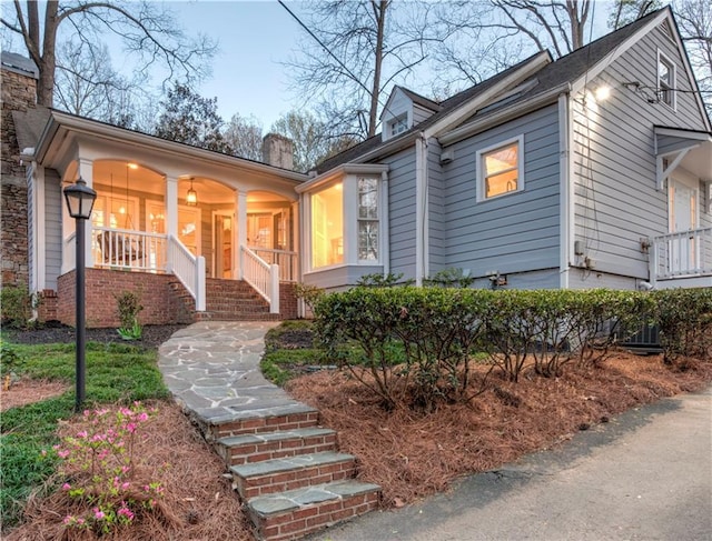 view of front of home with covered porch, stairway, and a chimney