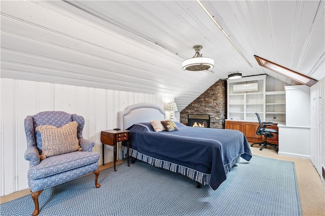 carpeted bedroom with a stone fireplace, lofted ceiling with skylight, and a wall unit AC