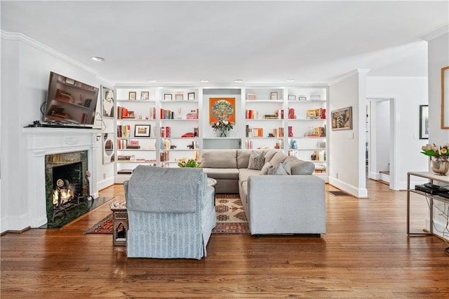 living room with built in shelves, a high end fireplace, crown molding, and wood finished floors