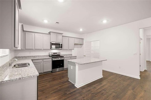 kitchen featuring sink, appliances with stainless steel finishes, light stone counters, a kitchen island, and dark hardwood / wood-style flooring