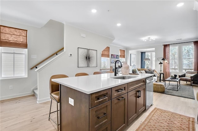 kitchen featuring a kitchen bar, light wood-type flooring, a sink, open floor plan, and dishwasher