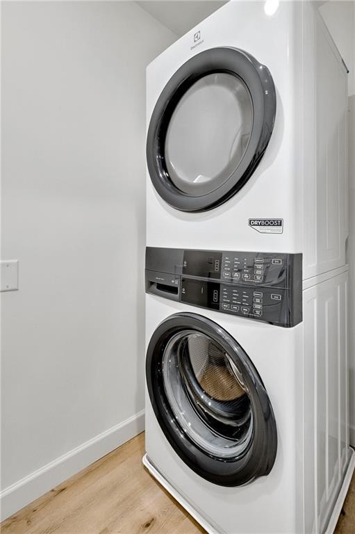 laundry area with baseboards, cabinet space, stacked washer and clothes dryer, and wood finished floors