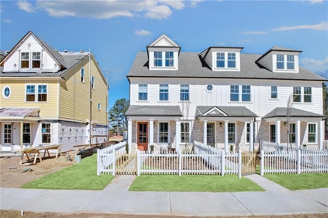 view of front of property featuring a fenced front yard, board and batten siding, a front yard, and roof with shingles