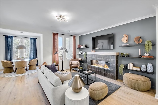 living room with a tiled fireplace, crown molding, baseboards, and wood finished floors