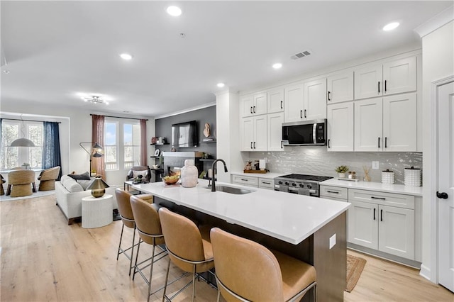 kitchen with visible vents, open floor plan, decorative backsplash, stainless steel appliances, and a sink