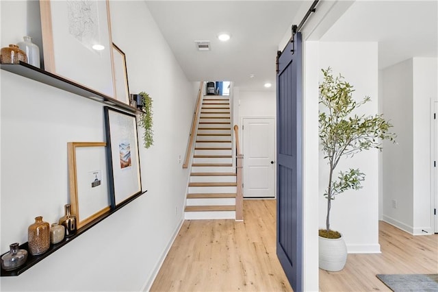 stairs with a barn door, wood finished floors, baseboards, and visible vents