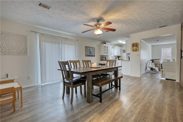 living room with ceiling fan, wood-type flooring, a brick fireplace, and a textured ceiling