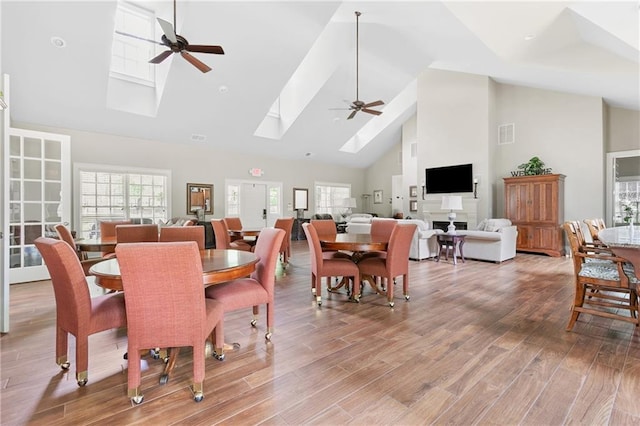 dining area with a ceiling fan, high vaulted ceiling, a skylight, and light wood-style floors