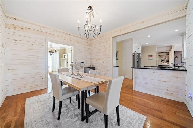 dining room featuring recessed lighting, an inviting chandelier, wood walls, and light wood finished floors