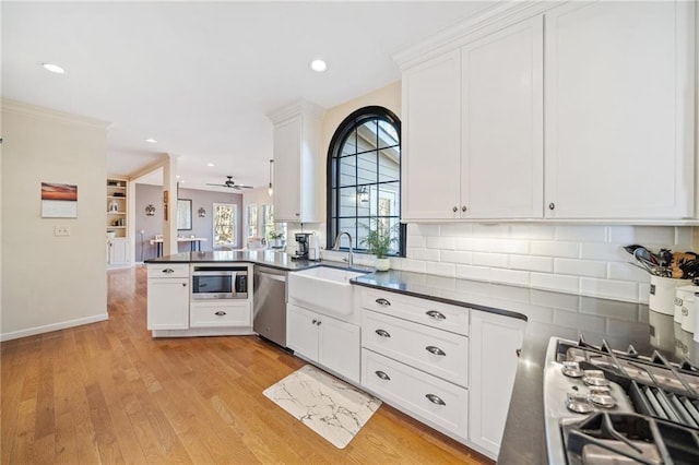 kitchen featuring a peninsula, stainless steel appliances, white cabinets, light wood-style floors, and dark countertops