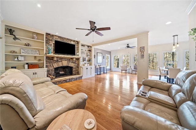 living area featuring a stone fireplace, crown molding, built in shelves, and light wood-style floors