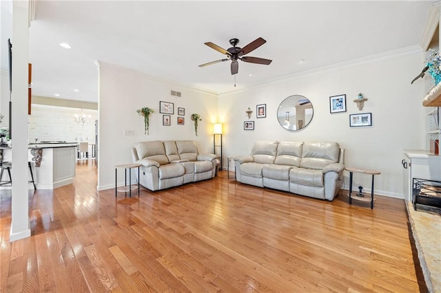 living room with ceiling fan with notable chandelier, crown molding, light wood-style floors, and baseboards