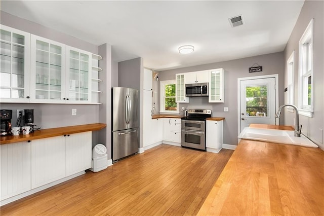 2486 Memorial Dr SE, Atlanta, GA 30317 - kitchen with appliances with stainless steel finishes, butcher block countertops, a sink, light wood finished floors, and white cabinetry