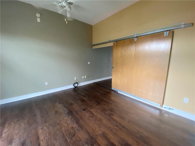 unfurnished room with ceiling fan, a barn door, and dark hardwood / wood-style flooring