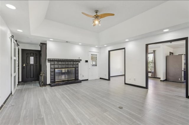 unfurnished living room with a barn door, recessed lighting, a fireplace, light wood-style floors, and a raised ceiling