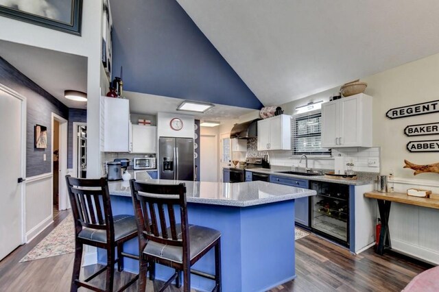 kitchen with white cabinetry, wall chimney exhaust hood, stainless steel appliances, a kitchen breakfast bar, and wine cooler