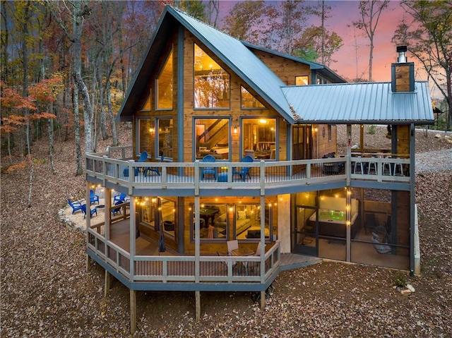 back of property at dusk with metal roof, a chimney, and a wooden deck