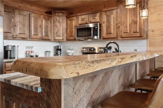 kitchen with a kitchen breakfast bar, hanging light fixtures, appliances with stainless steel finishes, decorative backsplash, and brown cabinetry