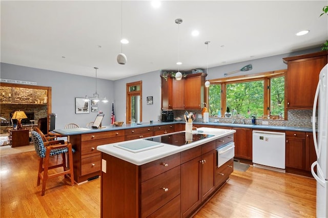 kitchen featuring white appliances, light hardwood / wood-style floors, a kitchen island, decorative light fixtures, and kitchen peninsula