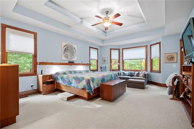 bedroom with light colored carpet, a tray ceiling, and multiple windows