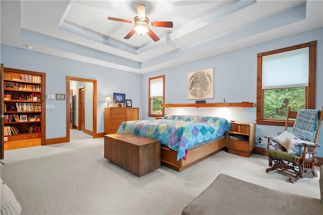 carpeted bedroom with a raised ceiling and ceiling fan