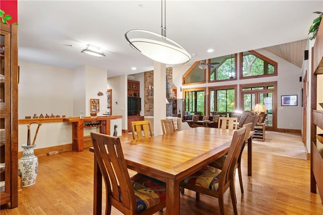 dining space featuring high vaulted ceiling, a fireplace, and light hardwood / wood-style floors