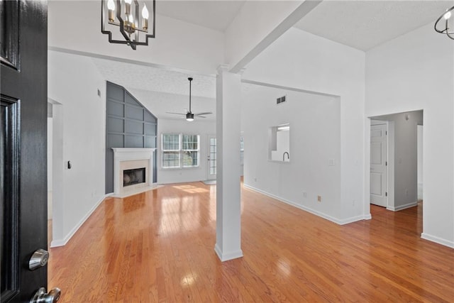 unfurnished living room featuring visible vents, light wood-style flooring, ornate columns, a fireplace, and ceiling fan with notable chandelier