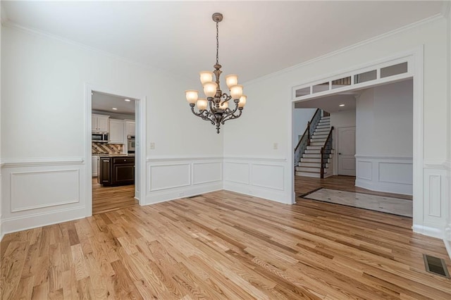 unfurnished dining area featuring an inviting chandelier, ornamental molding, and light wood-type flooring