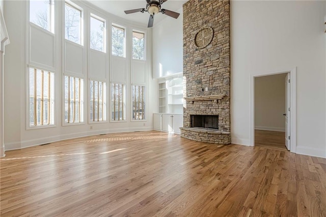 unfurnished living room with a stone fireplace, a wealth of natural light, ceiling fan, and light wood-type flooring