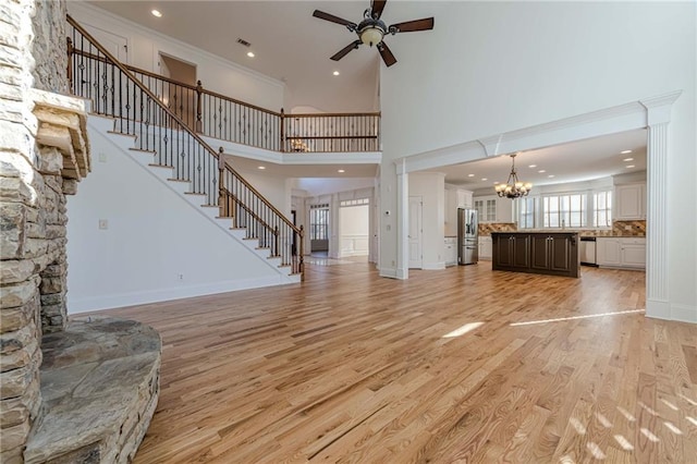 unfurnished living room featuring crown molding, ceiling fan with notable chandelier, light hardwood / wood-style flooring, and a high ceiling