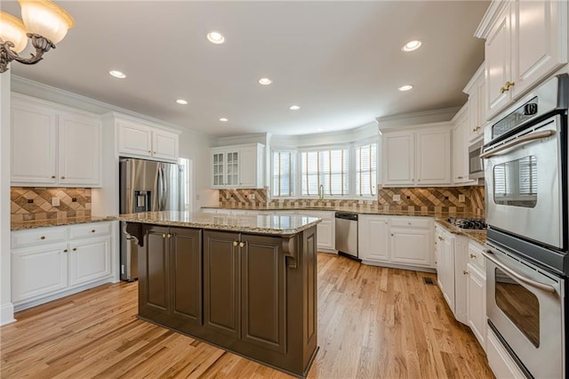 kitchen with light hardwood / wood-style flooring, appliances with stainless steel finishes, white cabinetry, light stone counters, and a kitchen island