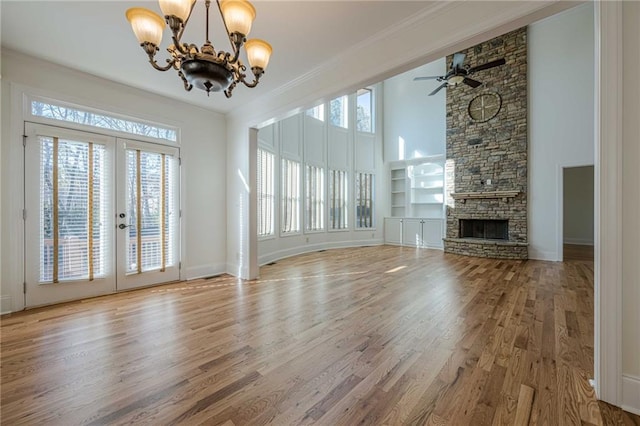 unfurnished living room featuring hardwood / wood-style floors, a fireplace, ornamental molding, ceiling fan with notable chandelier, and french doors