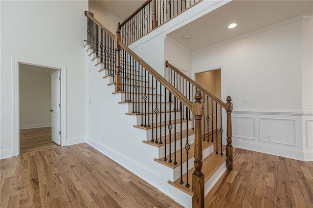 stairway with hardwood / wood-style flooring, a towering ceiling, and ornamental molding