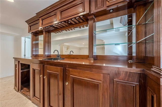 bar with decorative columns, sink, light tile patterned floors, and wooden counters