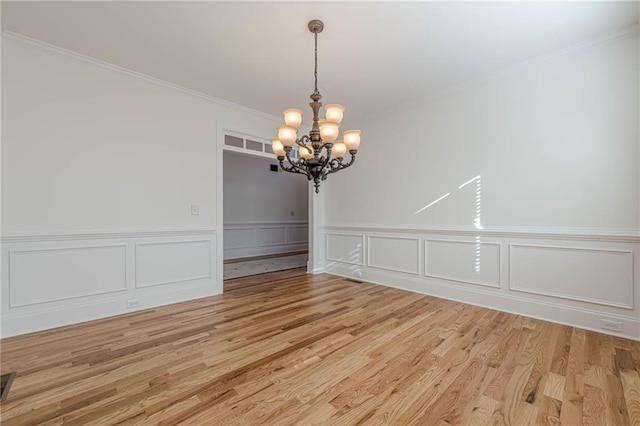 unfurnished dining area featuring an inviting chandelier, crown molding, and light hardwood / wood-style floors