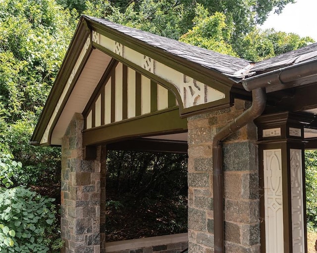 exterior space featuring a downspout, gutters, stone siding, and a shingled roof